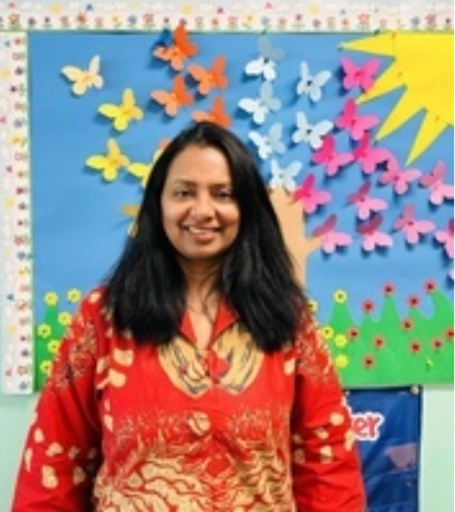 a woman with medium length hair wearing a red and gold blouse standing in front of a bulletin board with paper butterflies